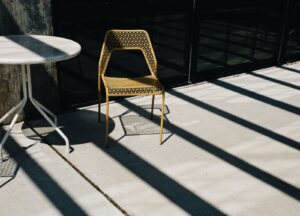 Sunlit concrete patio with a metal chair and table casting long shadows