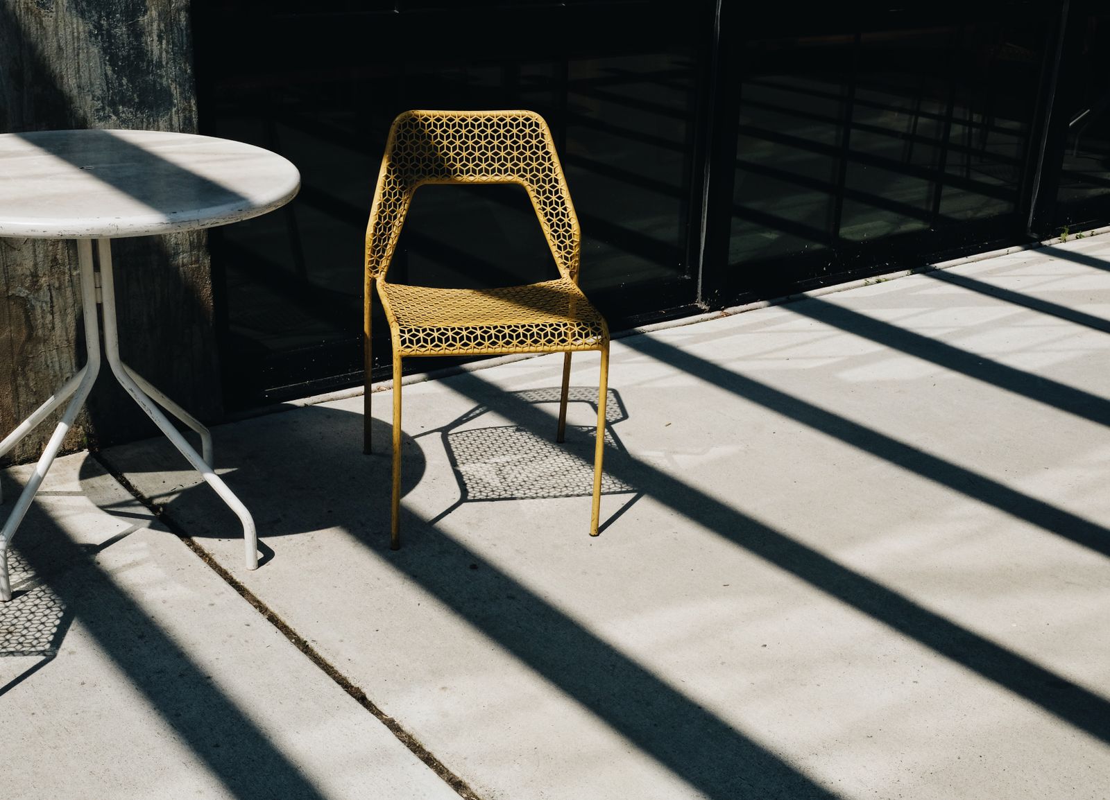 Sunlit concrete patio with a metal chair and table casting long shadows