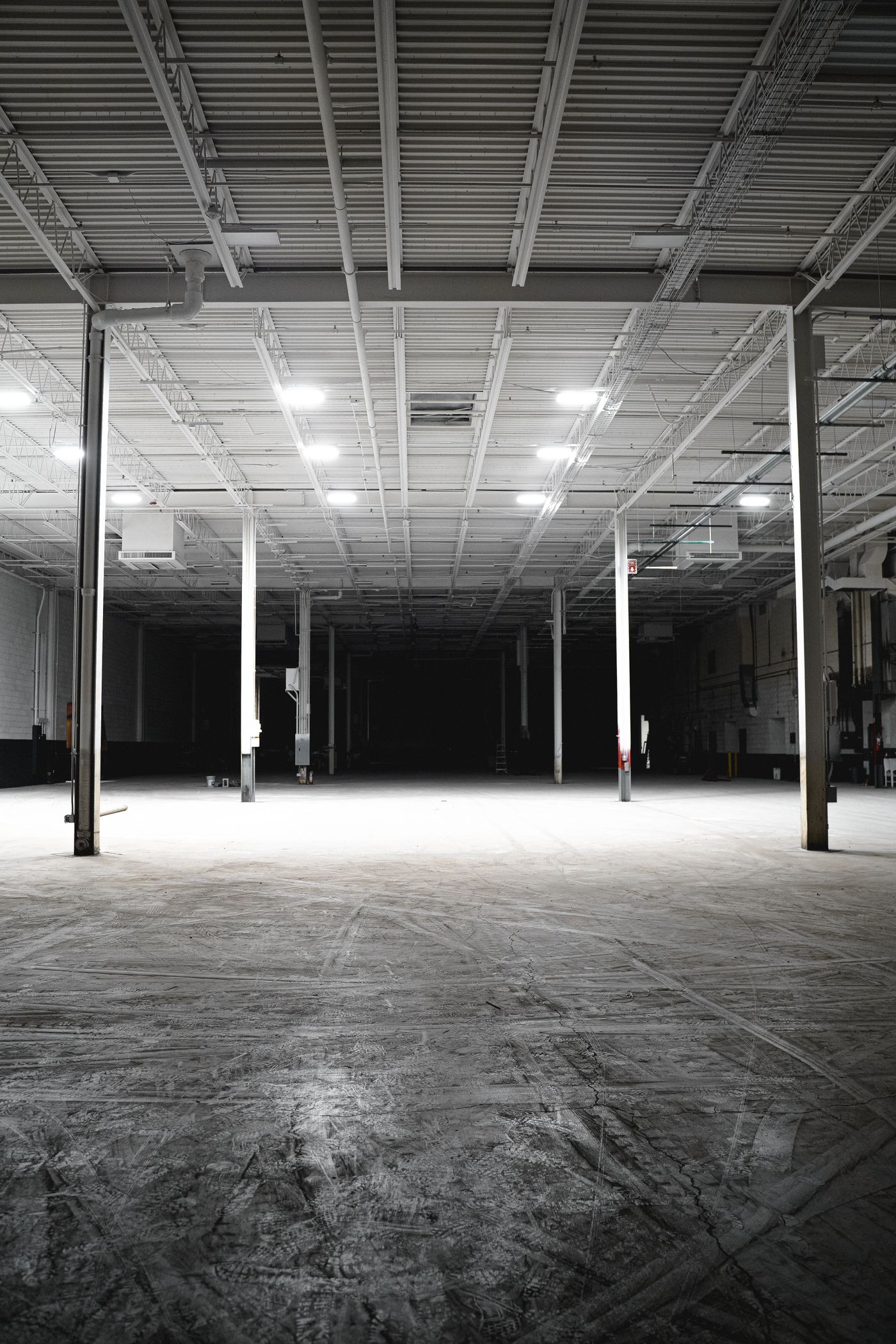 Empty warehouse interior with bright overhead lighting and an open concrete floor