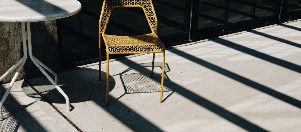 Sunlit concrete patio with a metal chair and table casting long shadows