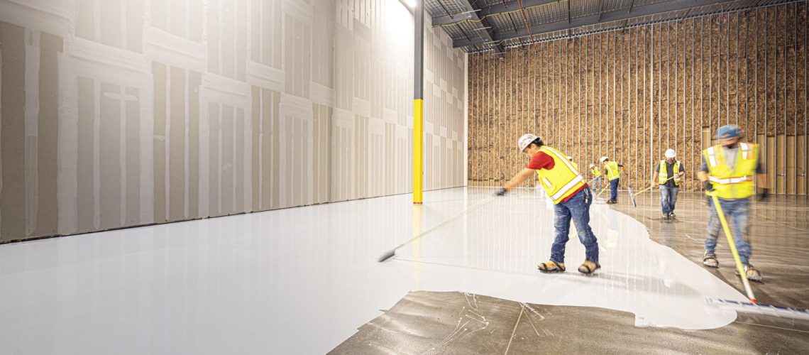 Crew spreading a fresh floor coating across a bare concrete slab in a commercial building